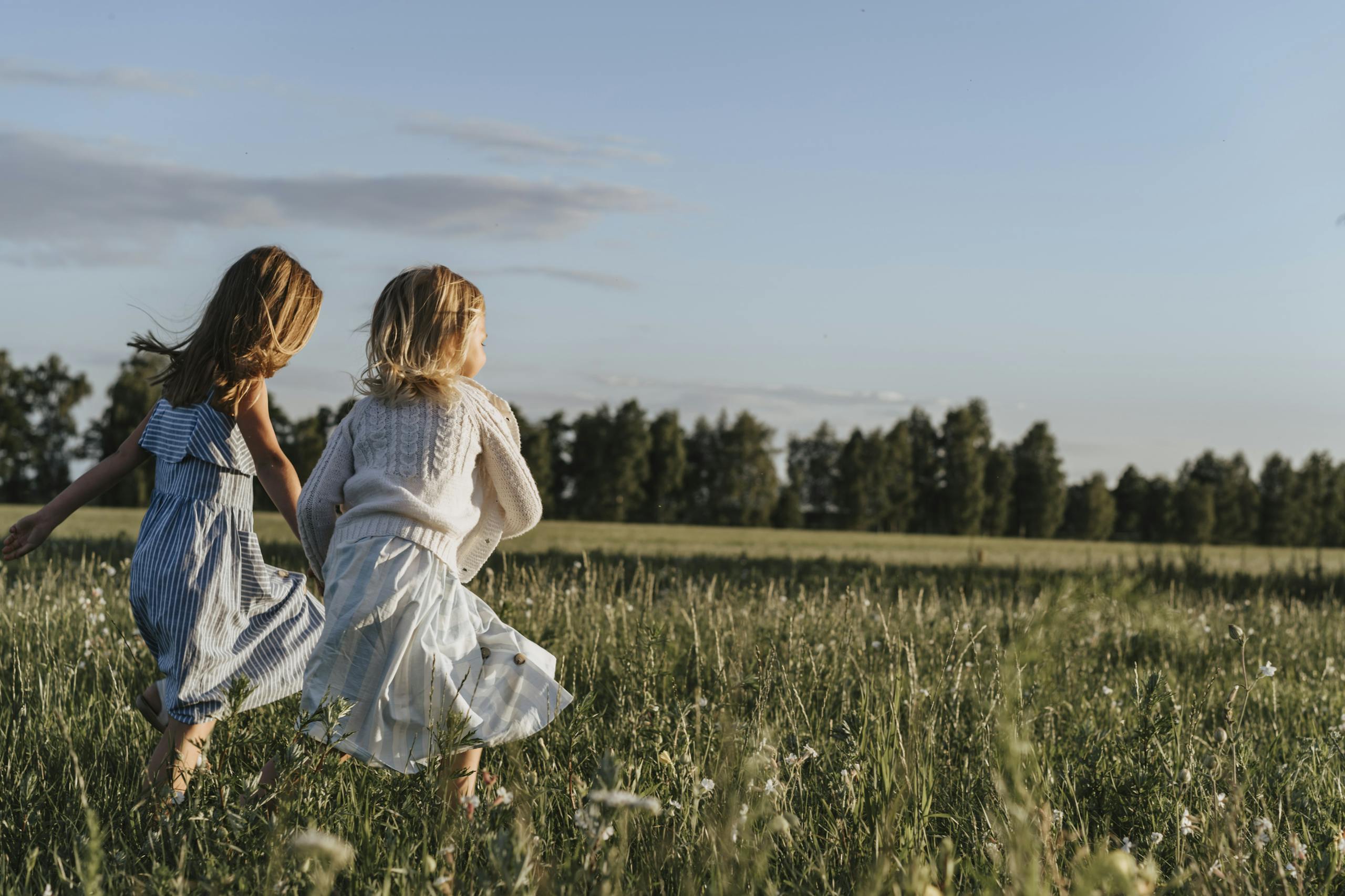 Two young girls joyfully running through a sunlit field, enjoying the outdoors.