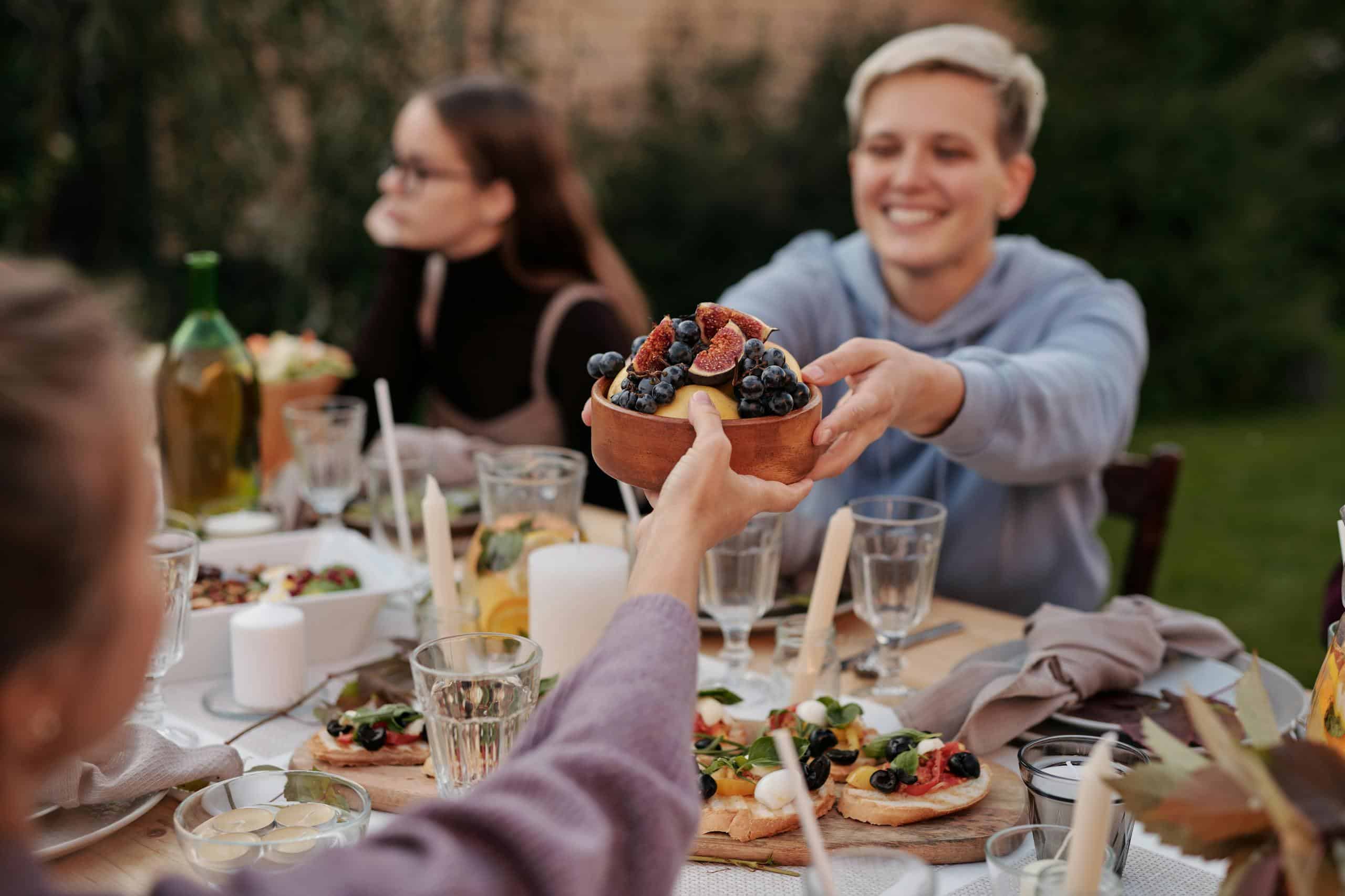 A group of friends enjoying an outdoor dinner, sharing a bowl of fruit in a garden setting.